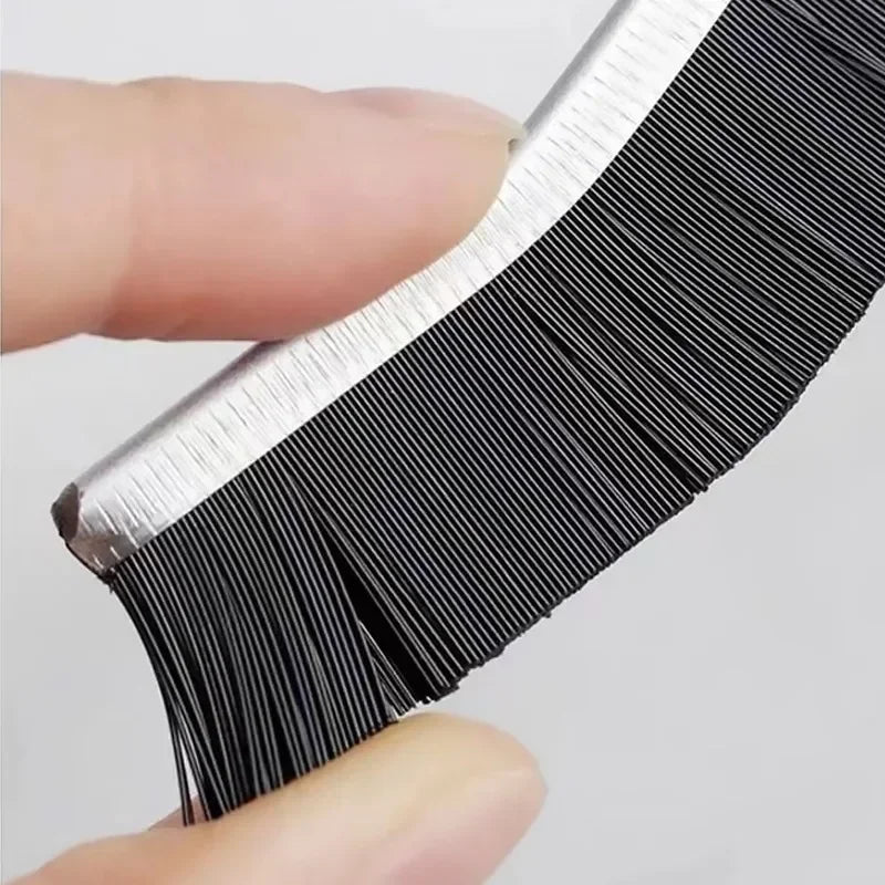A hand holds a black and silver grout gap cleaning brush set with fine bristles.