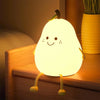 A glowing yellow silicone pear shaped night light resting on a wooden bedside table.