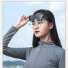 A woman wearing black sunglasses and eyeglasses is shown outdoors against a light blue sky.