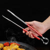 A hand holds a pair of stainless steel BBQ grill tongs and kitchen clips over food being grilled.