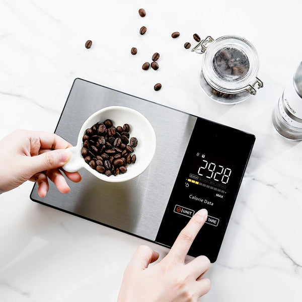 Hände verwenden eine digitale Küchenwaage, um Kaffeebohnen auf einer Marmoroberfläche abzumessen.