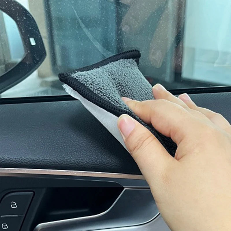 A hand is using a black microfiber detailing sponge on a car window.