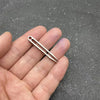 A hand holds a titanium clip tweezers with pointed tips against a dark gray textured background.