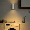 A modern white RGB motion sensor wall light illuminates a laundry room area above a countertop.