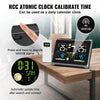 A digital clock and weather monitor device is shown on a wooden table with a hand interacting with it.