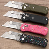 A collection of five folding steel utility knives with various colored handles and blades displayed on a wooden surface.