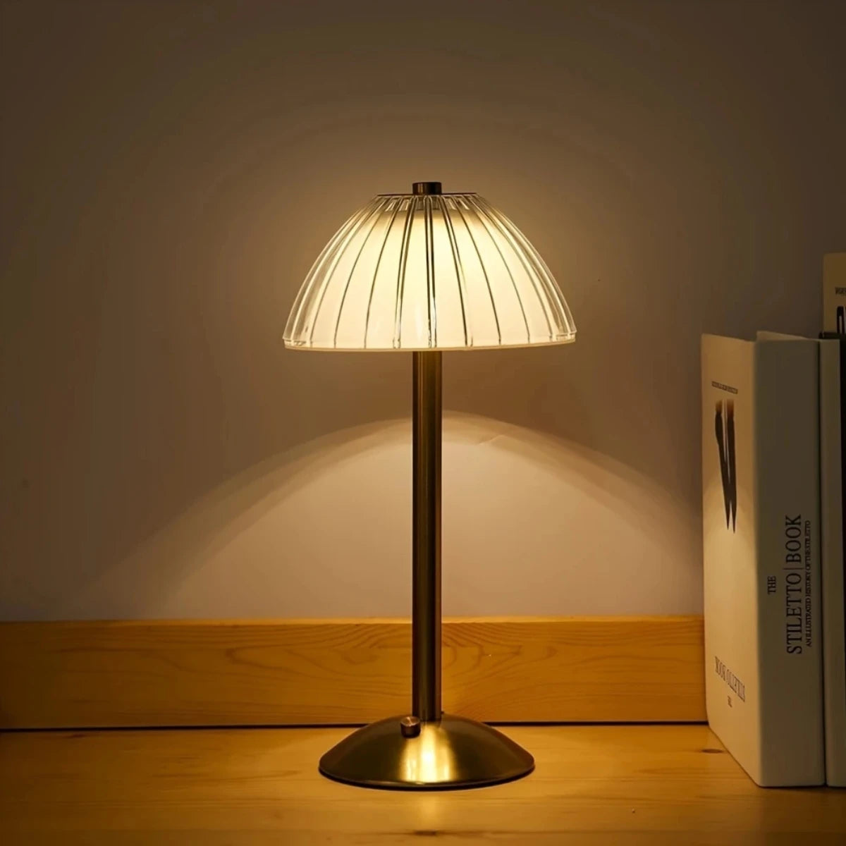 A modern table lamp with a conical glass shade and brass base illuminates a wooden surface.