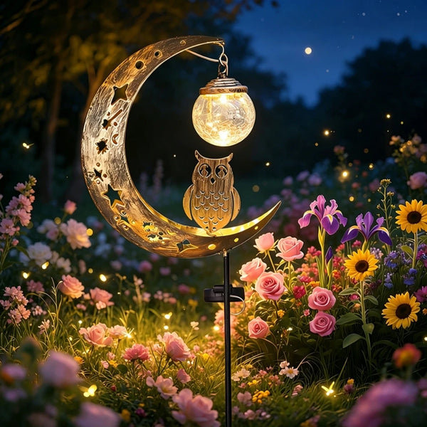 A golden crescent moon with an owl silhouette holds a glowing light, set in a garden pathway at twilight.
