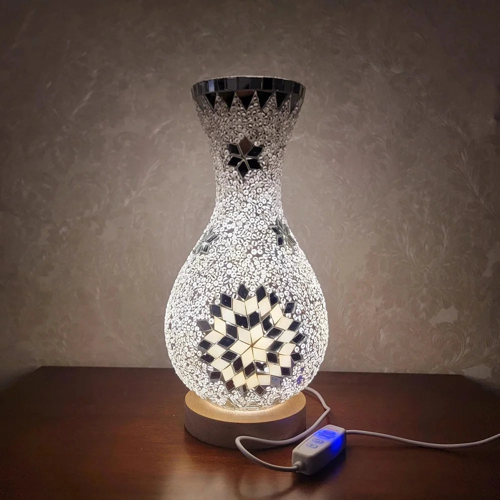 Lámpara de mesa de vidrio decorativa con diseño facetado y patrón iluminado sobre una superficie de madera.
