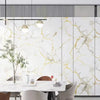 Comedor moderno con mesa y sillas de mármol blanco contra una pared de papel contact de mármol veteado en oro.