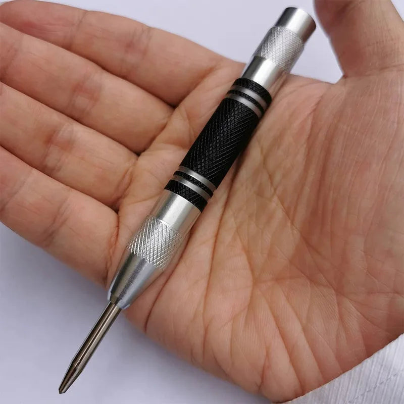 A hand holds an automatic centre punch tool with a silver body and black grip, showing the tip.