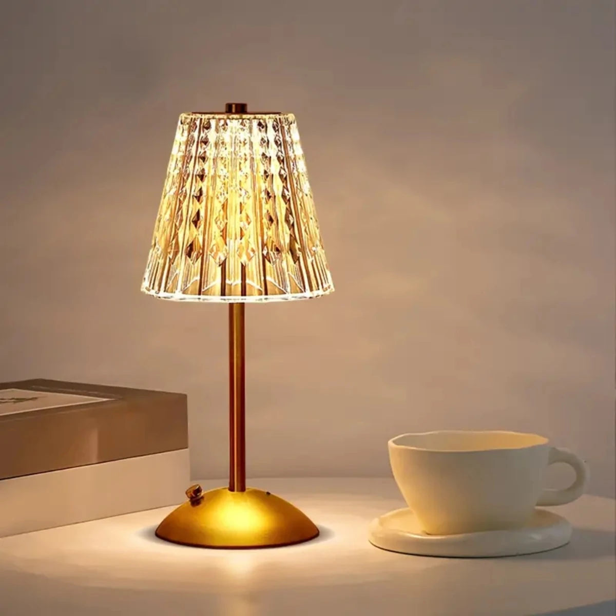 A brass table lamp with a textured glass shade illuminates a white cup on a light surface.