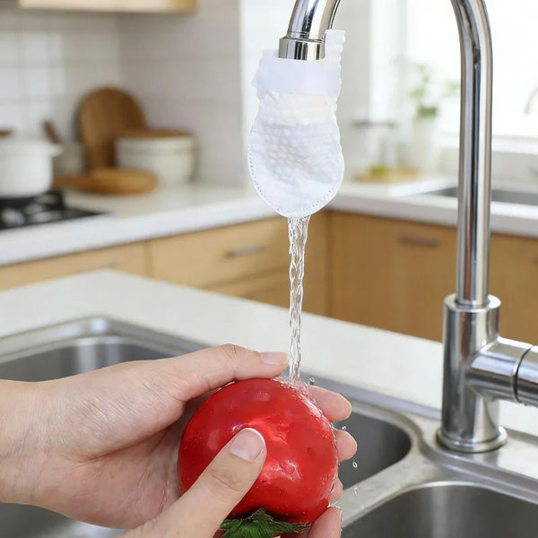 A hand is holding a red tomato under a faucet, which has a reusable cotton filter attached to the spout.