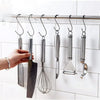 A hand hangs a set of stainless steel multipurpose hanging kitchen tools, including a knife, whisk, and ladle, from a bar.