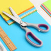 A pair of professional stainless steel sewing shears lying on a blue surface next to colorful paper and a ruler.