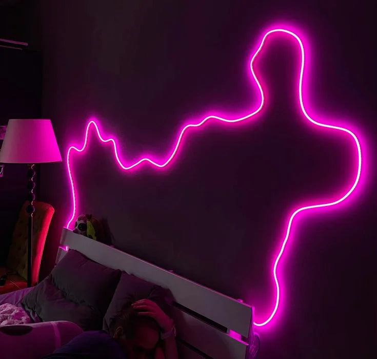 A silhouette of a person glowing in neon pink light on a dark wall above a bed.