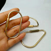 Eine Hand hält drei Messing-Gold-Schlüsselring-Karabinerclips vor weißem Hintergrund.