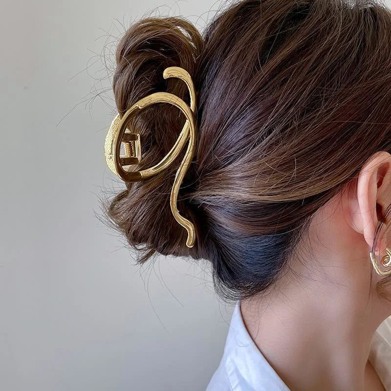 Elegant gold S-shaped metal hair clips used to style a dark brown updo