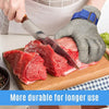 A hand wearing a stainless steel anti-cut safety glove is shown gripping a piece of fish on a wooden cutting board.