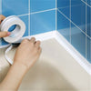 Une main applique du ruban d'étanchéité PVC blanc sur le bord d'une baignoire ou d'un lavabo carrelé bleu.