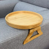 A round natural wooden tray with a handle rests on a gray sofa cushion.