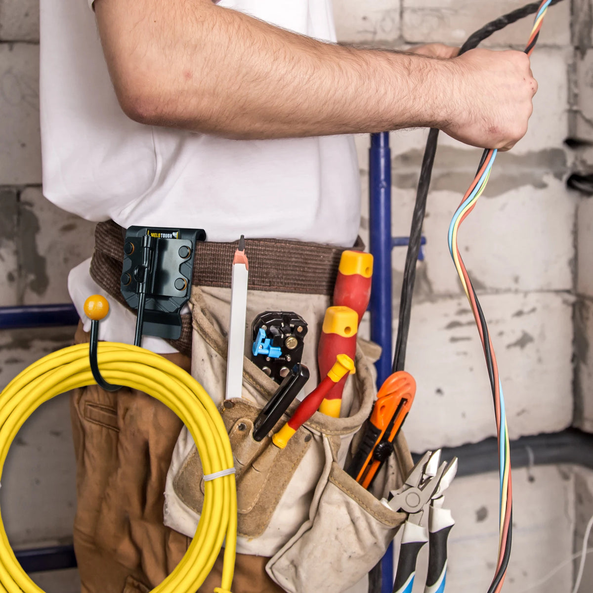 A person is holding a heavy-duty tool belt with various tools and a hook/holster for cordless drills.