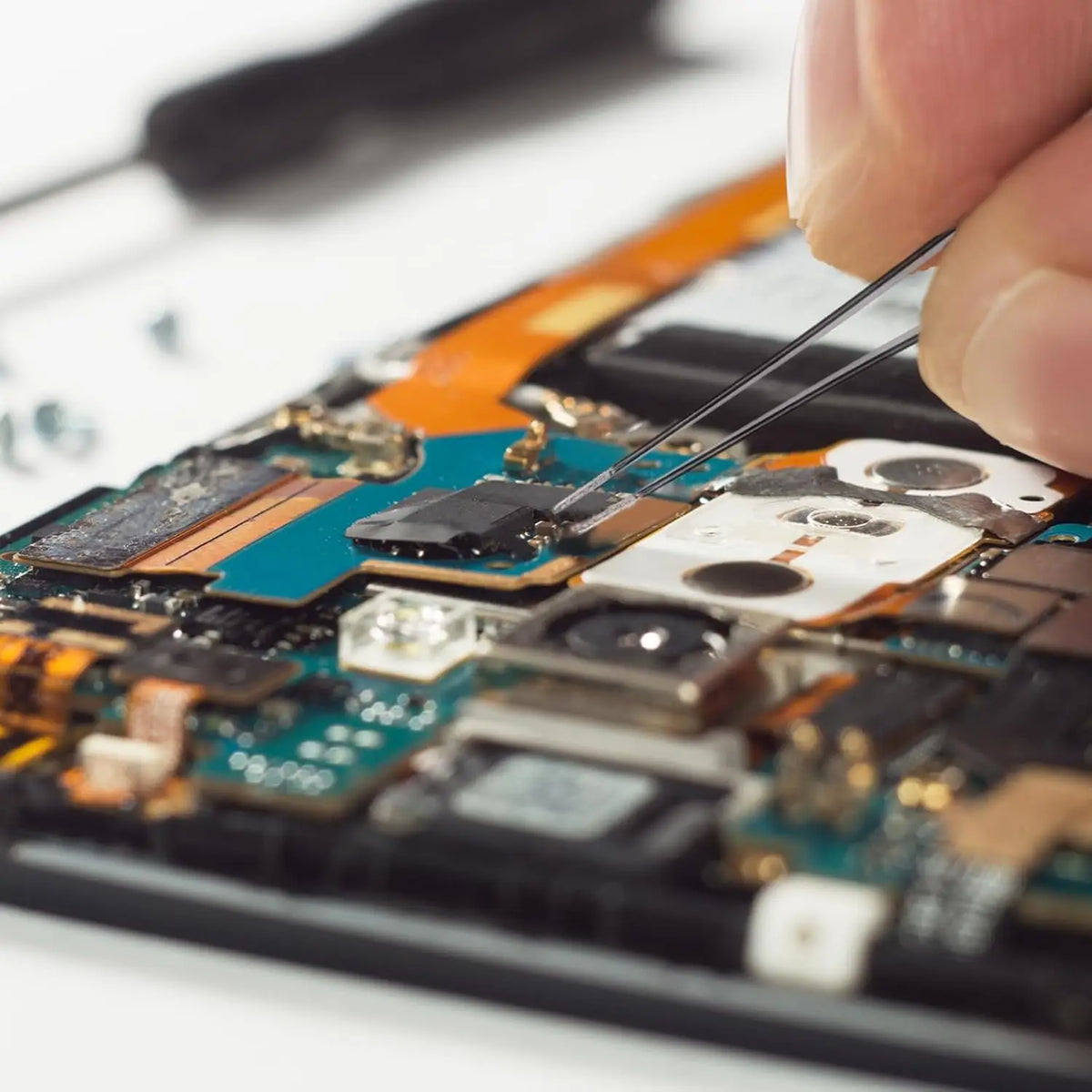 A hand uses precision tweezers to manipulate components on a circuit board.