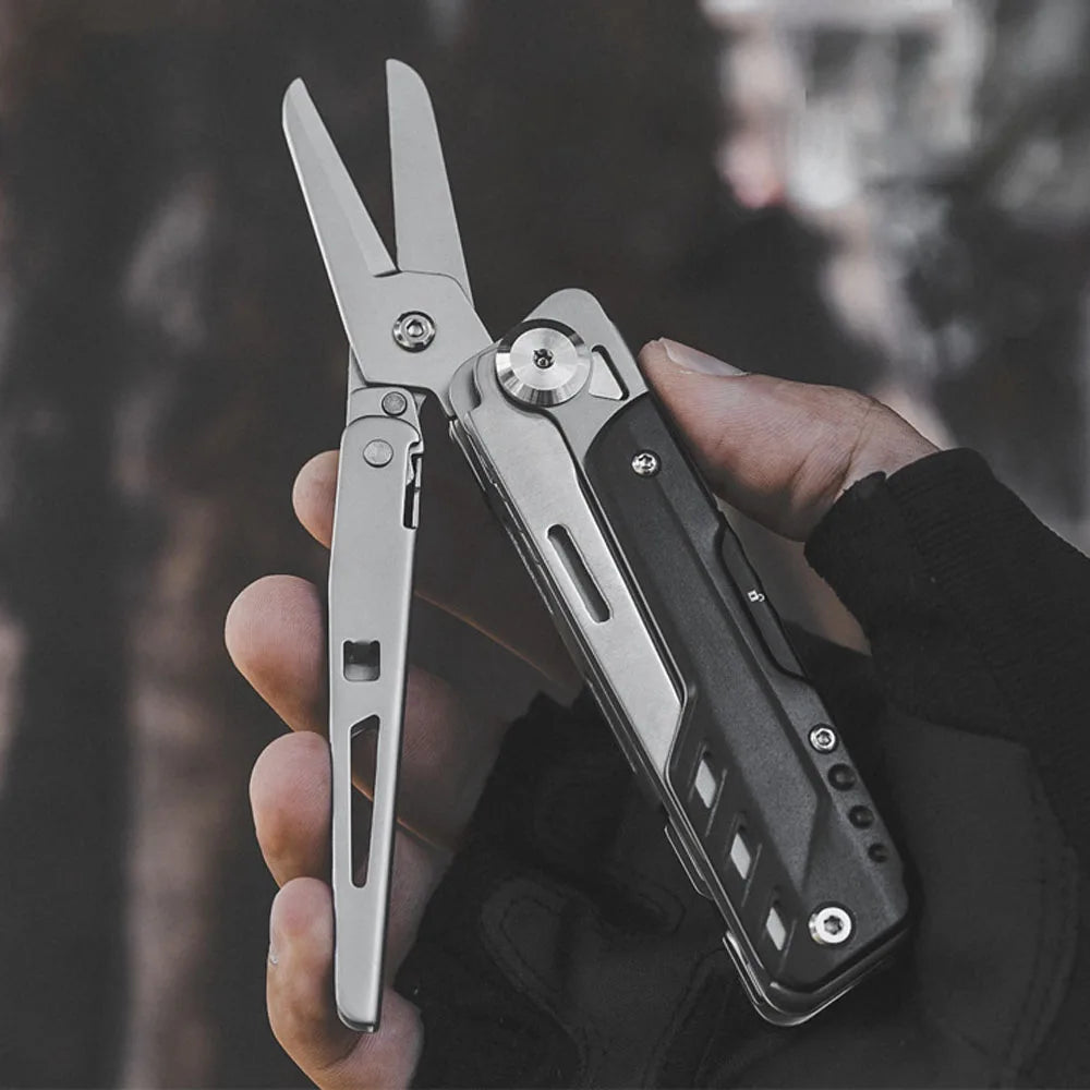 A hand holds a silver compact multi-tool pocket knife set against a blurred outdoor background.