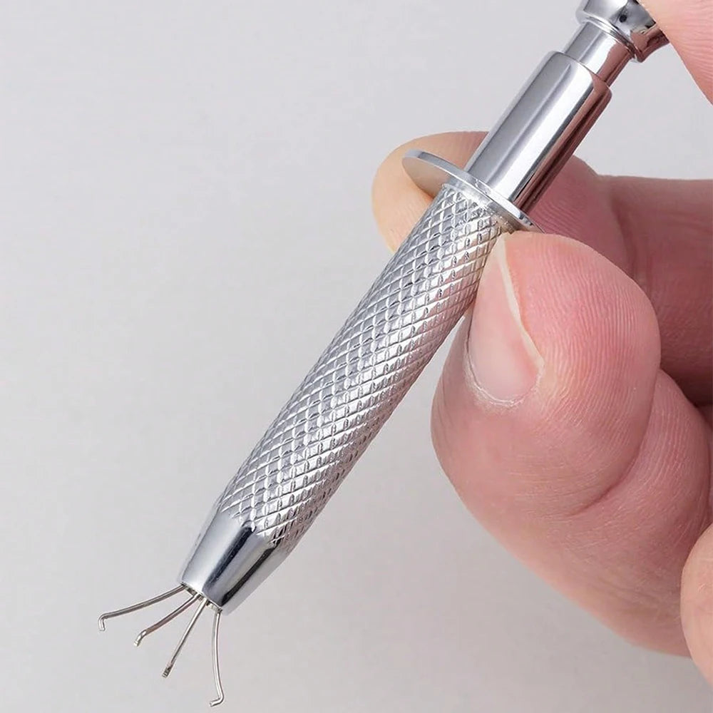 A hand holds a stainless steel piercing ball grabber kit with a textured handle and multiple prongs.