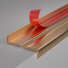 A close-up view of an L-shaped metal wall corner strip in a copper or bronze finish with a red accent piece.