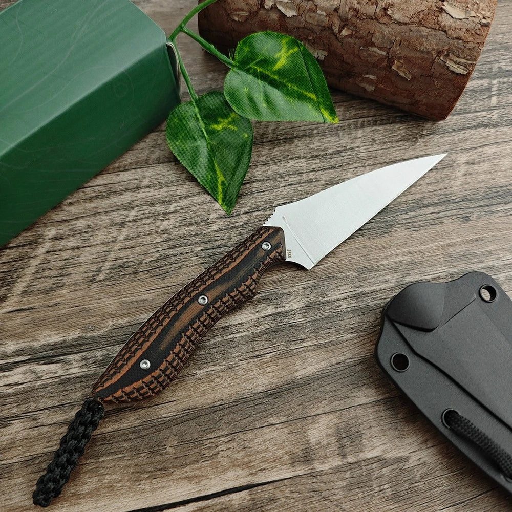 A compact fixed blade utility knife with a wooden handle and silver blade resting on a rustic wooden surface next to a green 