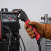 Eine Hand mit Lederhandschuh hält einen schwarzen und roten professionellen Kupfer-Schweißelektrodenhalter.