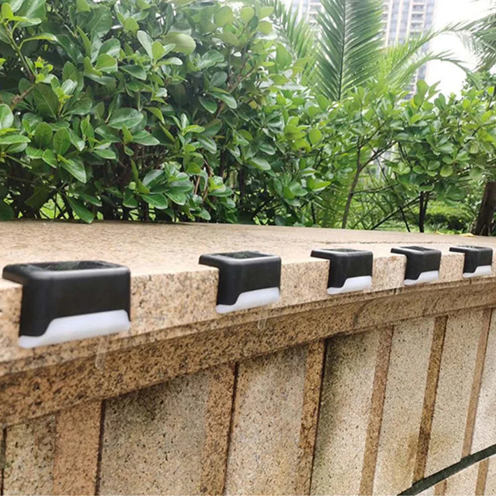 A row of solar powered deck and pathway lights mounted on a textured stone wall surrounded by lush greenery.