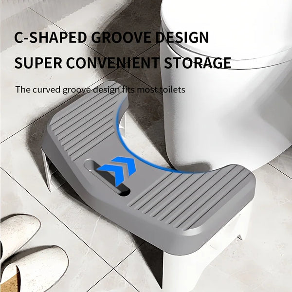 A gray toilet footstool with a C-shaped groove design is shown next to a white toilet bowl.