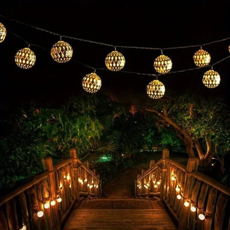 Luces de cuerda marroquíes iluminan un camino de madera rodeado de exuberante vegetación por la noche.