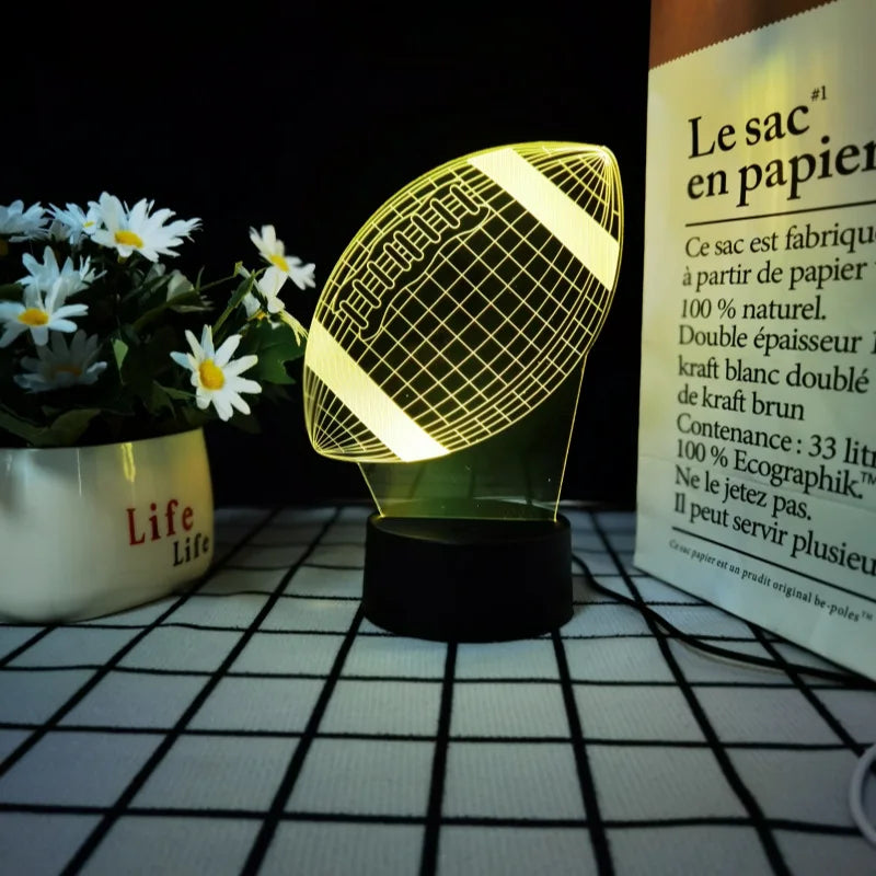 Una luz nocturna deportiva amarilla con patrón de malla sobre una superficie a cuadros blanca junto a una planta en maceta.