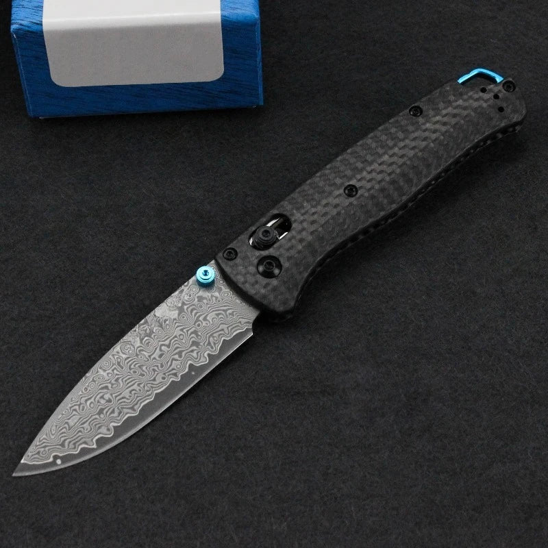 A black Damascus steel folding hunting knife with a textured handle and a silver blade is displayed on a dark surface.