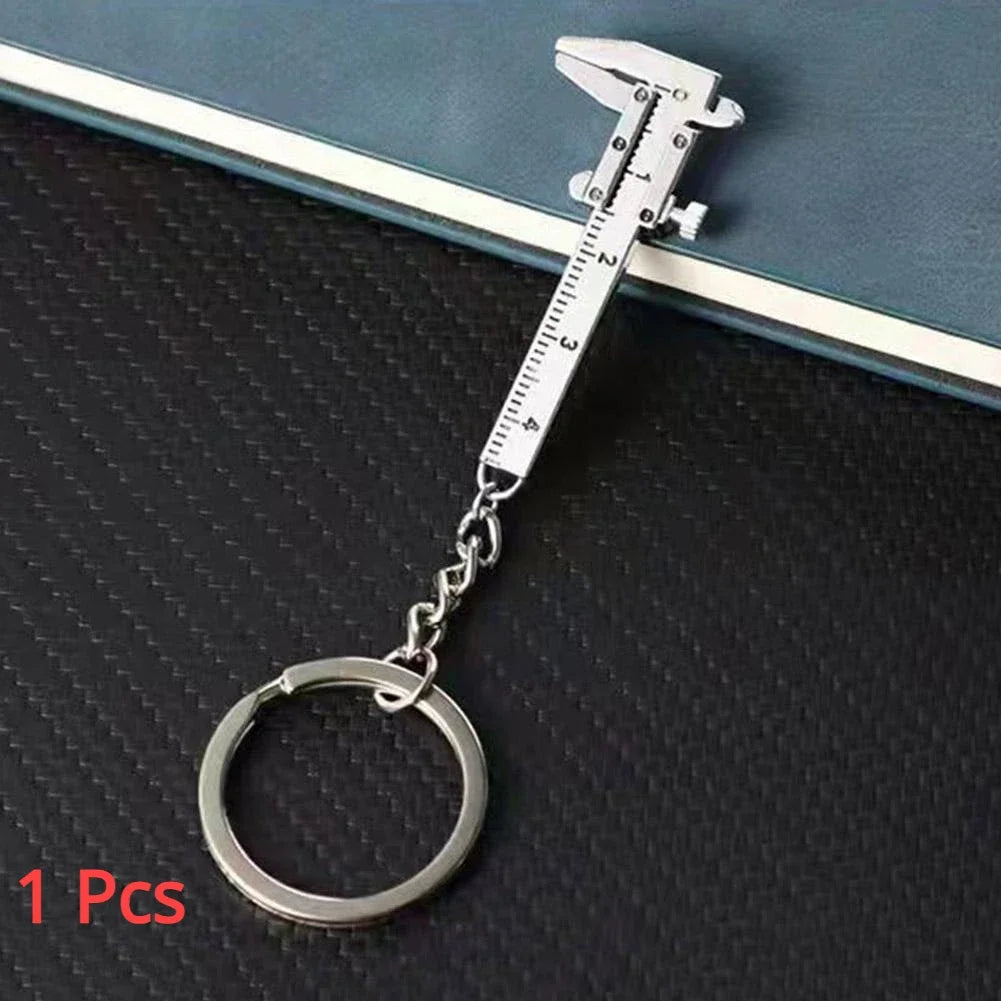 A silver metal jewelry measuring ruler and caliper keychain with a circular loop.