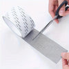 A hand is using scissors to cut a piece of reusable mosquito net repair tape for screens.