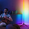 An RGB Dreamcolor floor lamp illuminates a room, with a man playing an acoustic guitar nearby.