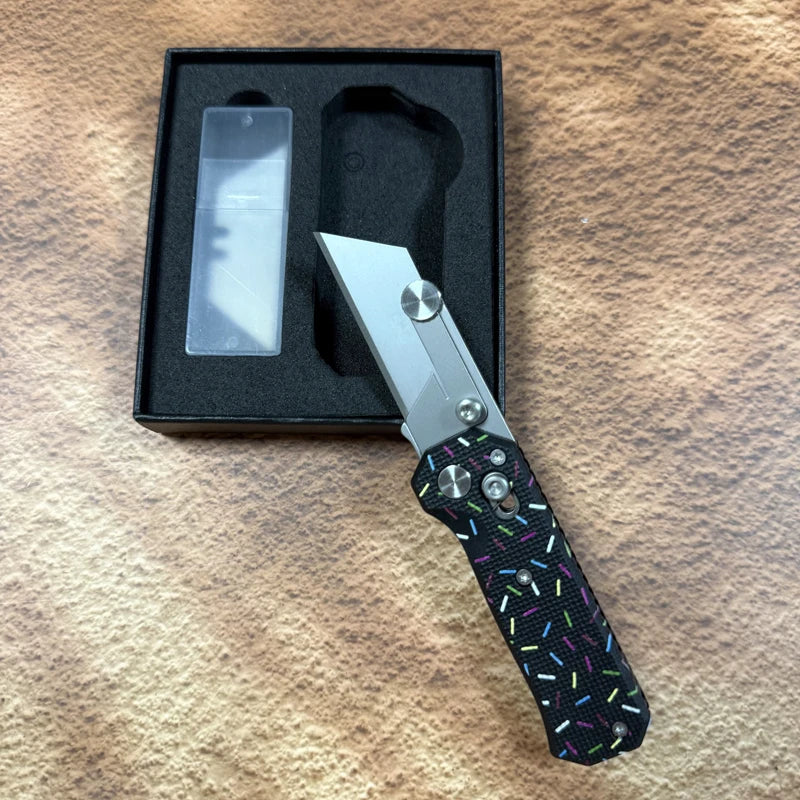 A folding utility knife with a stainless steel blade is displayed in its black box on a brown surface.
