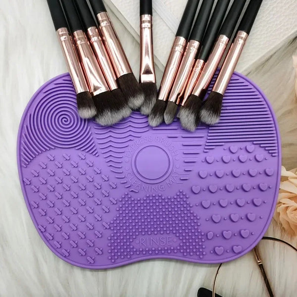 A purple silicone makeup brush cleaning mat with several pink and black makeup brushes resting on it.