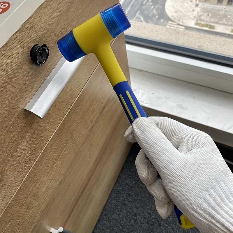 A hand wearing a white glove holds a yellow and blue rubber and plastic hammer set against a wooden surface.