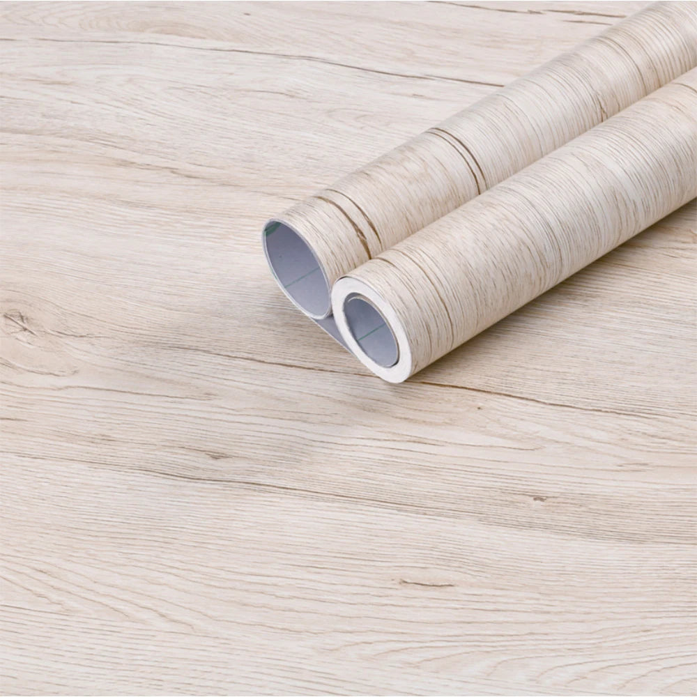 Two rolls of wood grain vinyl wall contact paper lying on a light wooden surface.