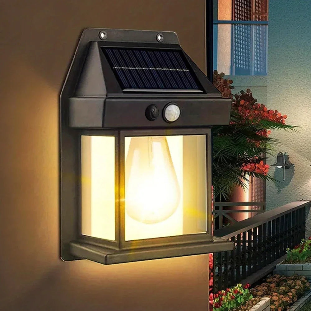 A black solar motion sensor LED wall light with a glass globe illuminates an outdoor area.
