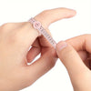 A hand is holding a pink precision ring measuring tool with a magnifier, showing the scale and ring size markings.