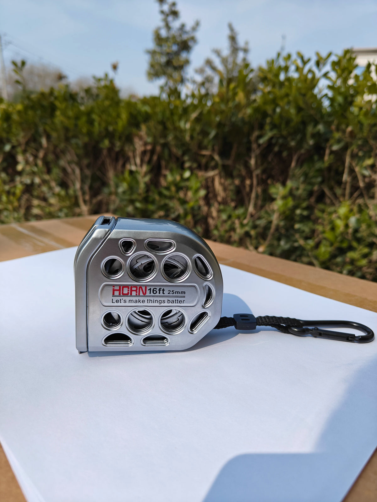 A silver heavy duty retractable metric tape measure with a black cord is displayed on a white surface.