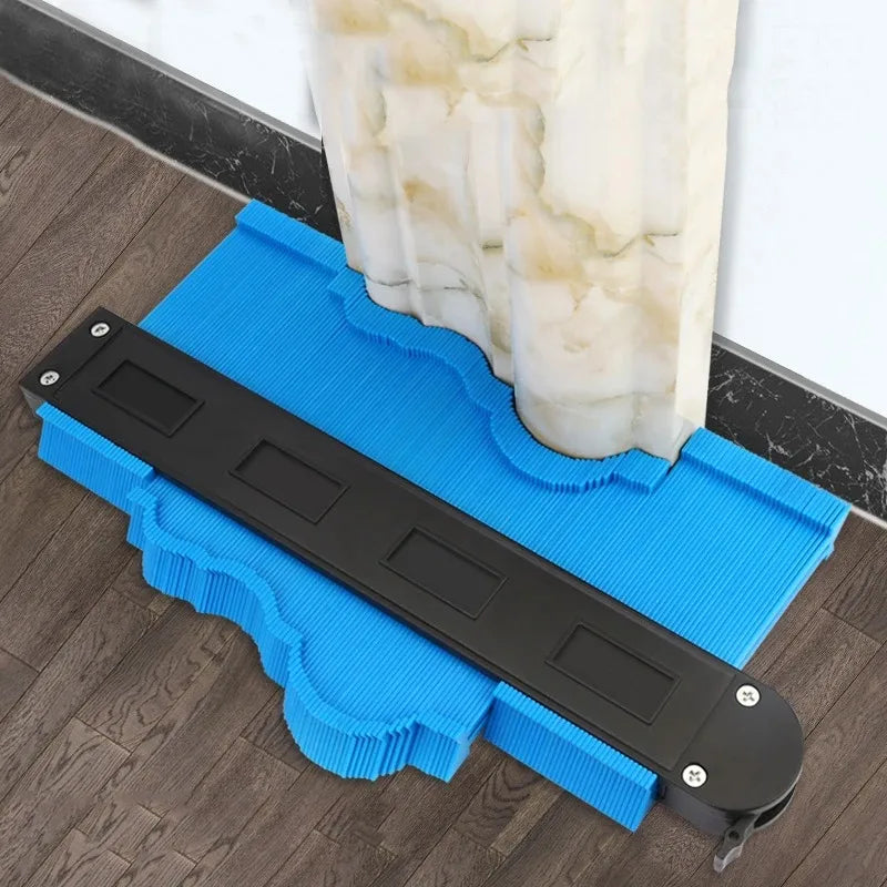 A black precision contour gauge and ruler is placed on a blue cutting mat next to a marble column.