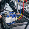 A blue refrigeration vacuum pump kit with gauges and tubing is installed in a car engine bay.