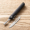 A black utility folding knife with a textured handle and a silver blade rests on a light wooden surface.